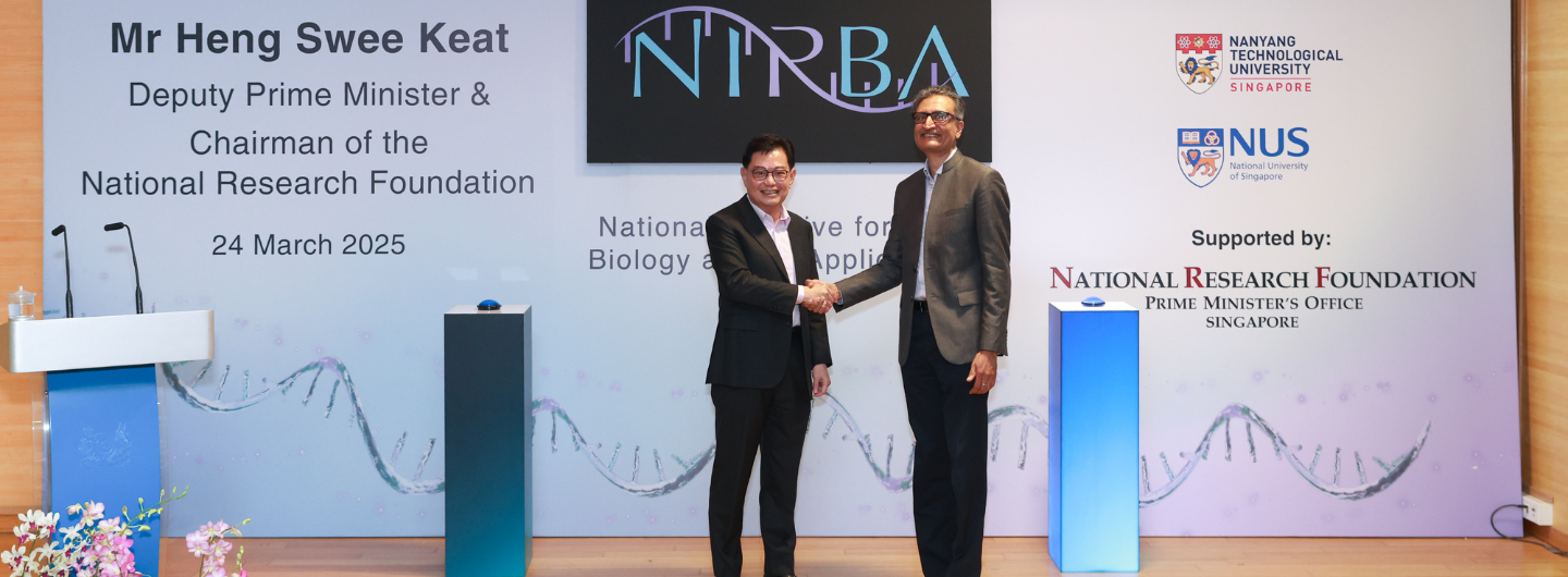 Two men in suits shake hands at a Nanyang Technological University & NUS event.